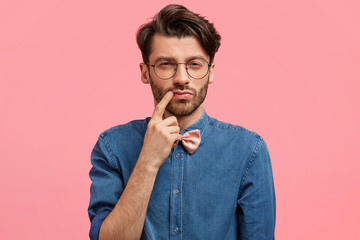Thoughtful stylish male student with pensive expression, contemplates how to make nice presentation...
