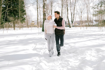 Fototapeta na wymiar Lovely couple together playing with snow outdoors on a sunny day. Pretty woman and attractive man wearing stylish casual clothes laughing and smiling each other.