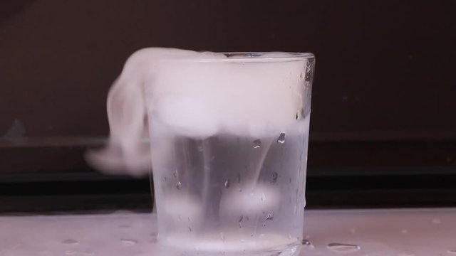 Dry ice in a glass of water and engender white smoke on white floor with black background.
