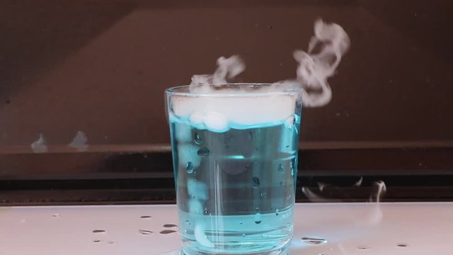 Dry ice in a glass of blue water and engender white smoke on dark background.