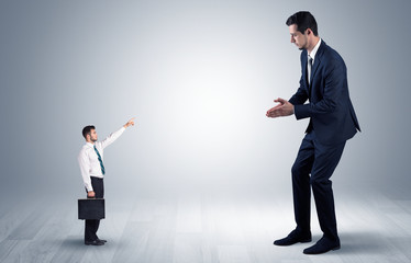 Small businessman in shirt pointing to an afraid businessman
