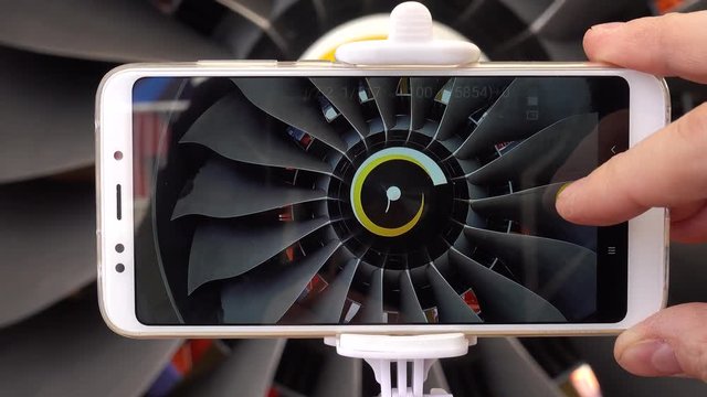 A man engineer photographs a jet engine. The man's hand takes a picture of the engine of the aircraft, using a modern smartphone and a monopod for selfie.