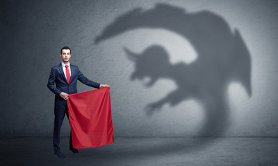 Businessman standing with red cloth in his hand and imp shadow on the background
