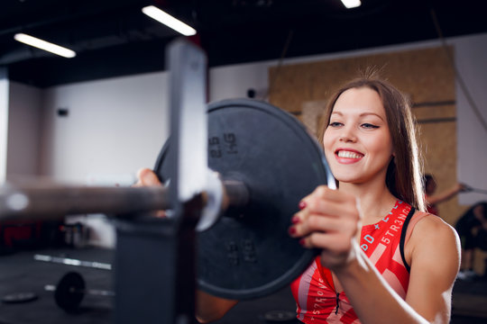 Image of smiling sportswoman in sports clothes with barbell