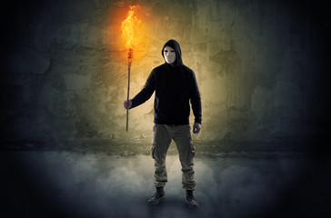 Ugly wayfarer with burning torch in his hand in front of a crumbly wall concept
