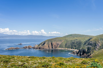 Obraz premium Beautiful view from light house station to stunning rocky cliffs bay and deep blue water of southern ocean on warm sunny day with blue sky after hiking to South Cape, Bruny Island, Tasmania, Australia