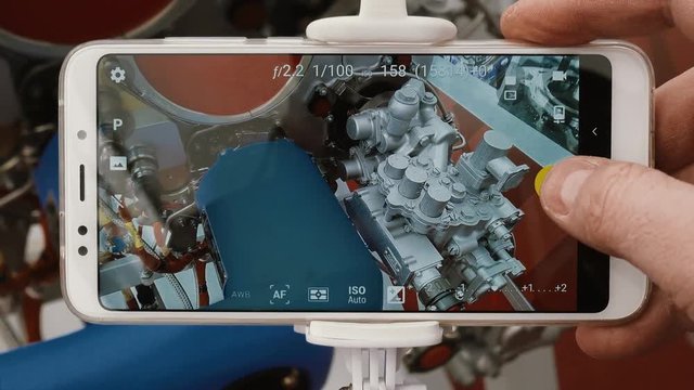 A student of a technical institute is studying an aircraft engine. Point of view. A man's hand takes a snapshot of a jet engine using a modern smartphone and selfie monopod.