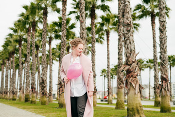 Fototapeta premium stylish attractive young woman in a coat holds a pink balloon and walks in the park