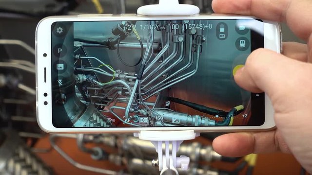 A man engineer photographs a jet engine. The man's hand takes a picture of the engine of the aircraft, using a modern smartphone and a monopod for selfie.