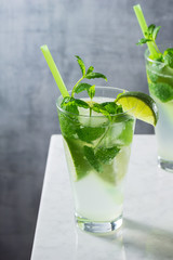 Two Cold Mojito Cocktails in Glasses Made with Mint, Lime, Rum, Simple Syrup, and Soda Water on Marble Bar Counter