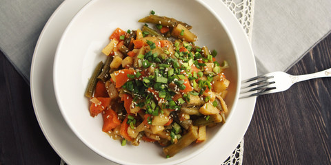 Vegetable stew with potato, carrot and green beans topped with sesame seeds. European cuisine. Healthy vegan lunch on the round white plate. European cuisine. Vegetarian. Top view. Wide photo.