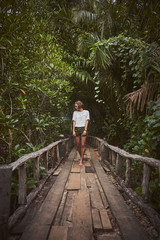 Fototapeta na wymiar Traveling girl on the wooden bridge. Pretty young woman in the jungle. Summer lifestyle and adventure photo