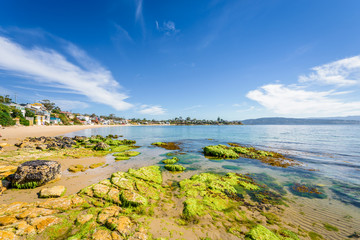 Pretty little to village town view with great paradise sandy beach with turquoise blue water and green covered rocks stone on warm sunny clear day for relaxing Opossum Bay, Hobart, Tasmania, Australia