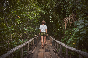 Naklejka na ściany i meble Traveling girl on the wooden bridge. Pretty young woman in the jungle. Summer lifestyle and adventure photo
