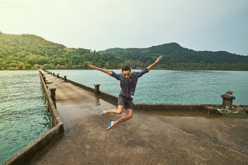 Traveling boy on the pier. Pretty young man jumping on the bridge. Summer lifestyle and adventure photo