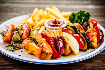 Kebabs - grilled meat with french fries and vegetables on wooden background