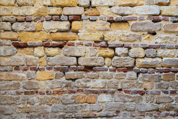 Background of irregular pattern of yellowish, red and gray grunge weathered uneven bricks stone wall surface