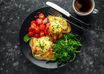 Eggs Benedict on english muffin with smoked salmon, wild rocket and hollandaise sauce in a black plate.