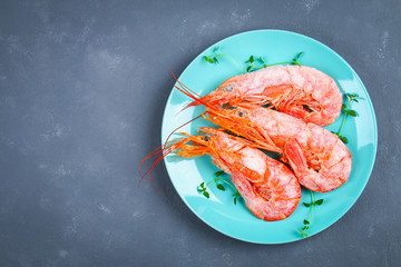 Large royal raw frozen prawns on a blue plate with thyme and basil on a concrete table. Red shrimps. Top view.