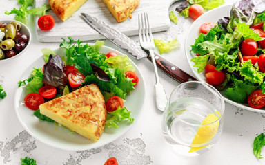 Spanish tortilla, omelette with potato, onion, vegetables, tomatoes, olives and herbs in a white plate. breakfast, healthy food.