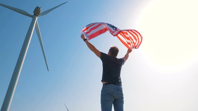 Native American boy with flag with stars and stripes near giant windmills in the field. Love to your country. Celebrating 4th July Independence Day. 4K in slow motion. American dream.