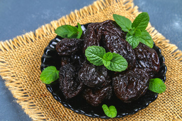 Prunes and fresh mint leaves in a bowl on a concrete table.