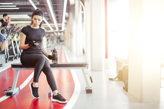 Fit young woman resting after hard training, drink water and looking at smartphone with exercise app