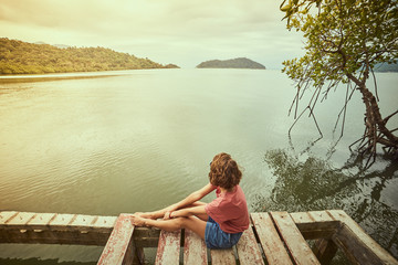 Fototapeta premium Traveling girl on the wood pier. Pretty young woman and tropical landscape. Summer lifestyle and adventure photo. Fish eye lens image