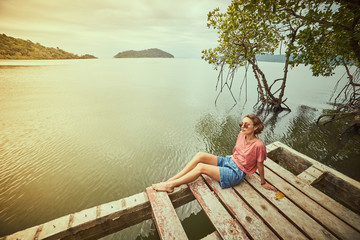 Traveling girl on the wood pier. Pretty young woman and tropical landscape. Summer lifestyle and adventure photo. Fish eye lens image