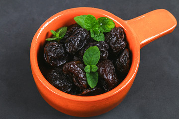 Prunes and fresh mint leaves in a bowl on a concrete table.