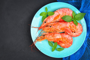Large royal raw frozen prawns on a blue plate with thyme and basil on a concrete table. Red shrimps. Top view.