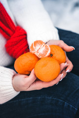 girl in white sweater and red scarf holds mandarins in her hands in the winter
