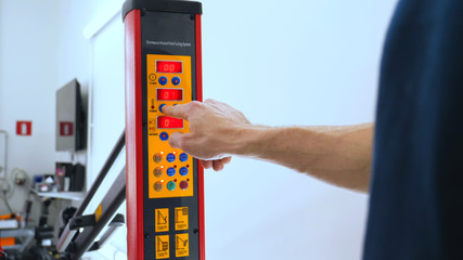 An employee professional adjusts the red ceramic lamps by pressing buttons to change temperature, auto workshop, car washing.