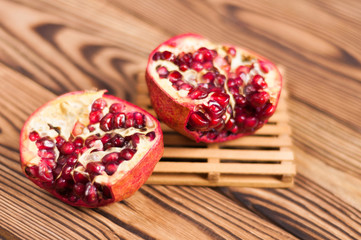 One half of red fresh ripe pomegranate with seeds on pallet beside one piece of pomegranate on old brown weathered wooden planks