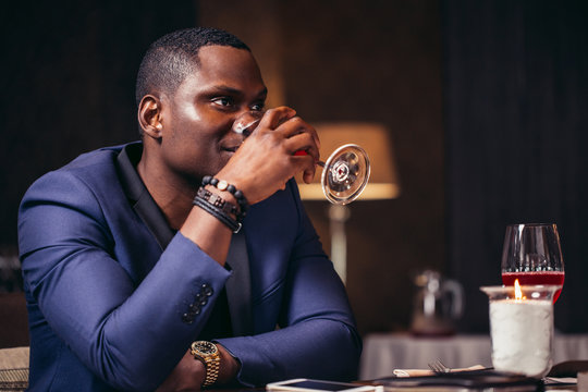 Handsome afroamerican man in blue jacket drinking wine at restaurant
