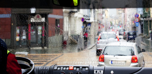 Obraz premium raindrops on the drivers bus window. clolful view on street traffic. urban backgruond.