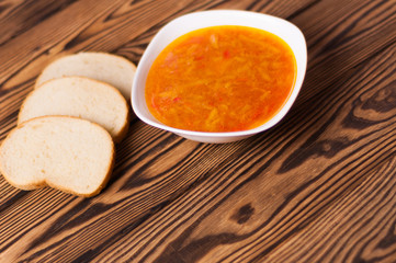 One full white ceramic bowl of fresh hot vegetable borscht and three pieces of bread on old weathered rustic wooden table. Ukrainian national food