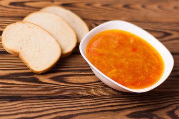 One full white ceramic bowl of fresh hot vegetable borscht and three pieces of bread on old weathered rustic wooden table. Ukrainian national food