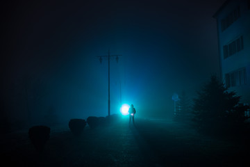 City at night in dense fog. Mystical landscape surreal lights with creepy man. The walking man's...