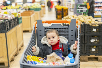 Boy 2 years in a supermarket, sitting in a cart full of various products