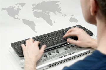 Blurred man in the foreground writing on keyboard, hands are on the move, world map in the background
