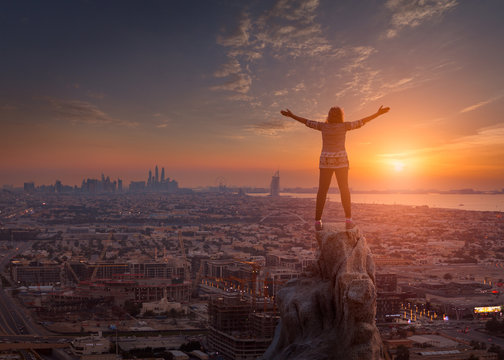 Women standing on the cliff towards the cityscape and setting sun