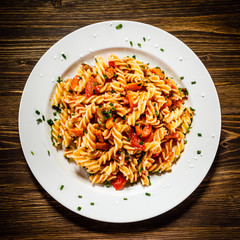 Pasta with tomato sauce and vegetables on wooden table