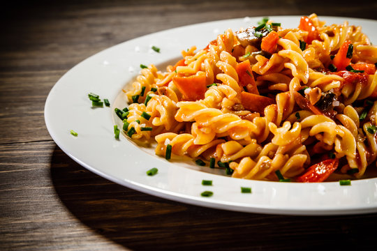 Pasta with tomato sauce and vegetables on wooden table