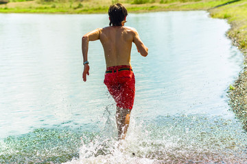 young korean man runs his back on the water with a smile and a naked torso
