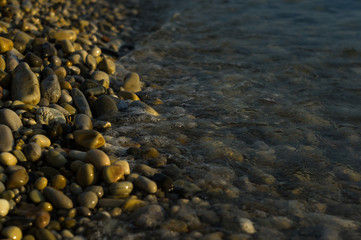 pebble stones on the sea beach, the rolling waves of the sea with foam