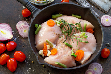 Fresh meat. Raw chicken fillet on a cast iron frying pan, spices and fresh vegetables on a kitchen table.