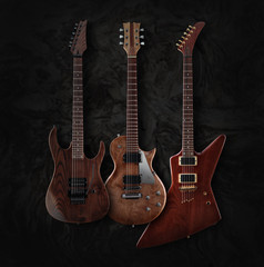 Set of three different shaped electric guitars with natural finish isolated on dark moire...