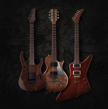 Set of three different shaped electric guitars with natural finish isolated on dark moire background, low key