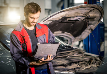 Professional car mechanic working in auto repair service with special laptop for automatic fix